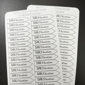 May include: A sheet of white sticker paper with black text that reads "DAILY devotion" printed in a repeating pattern. The stickers are shaped like arrows pointing to the right.