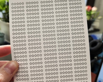 May include: A sheet of stickers featuring numerous black outline star shapes. The stickers are on a white background and held by a hand. The text "BEBLESSED STICKERS BY LORETTA-5 STARS ETSY.COM/SHOP/BEBLESSEDSTICKERS" is printed at the top.