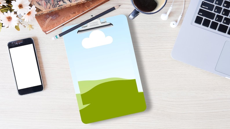 May include: A clipboard with a landscape design featuring a blue sky, white cloud, and green hills. A smartphone, a laptop, a cup of coffee, and a pencil are also on the light wood surface.