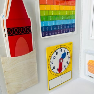 K&ouml;nnte beinhalten: Eine wei&szlig;e Tafel mit einem roten Stift, einer Bruchrechentafel mit Regenbogenfarben und einer gelben Uhr mit beweglichen Zeigern.