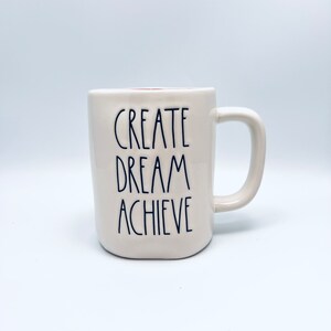 May include: White ceramic mug with a red rim and black text that reads "CREATE DREAM ACHIEVE".