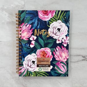 May include: A spiral-bound notebook with a floral design. The cover features pink and white flowers, green leaves, and the word "Notes" in gold lettering against a dark blue background. The notebook is labeled "Recycled".