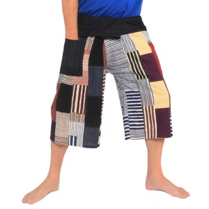 Può includere: Pantaloni in stile patchwork con un motivo geometrico colorato in tonalità di blu, marrone, rosso e giallo. I pantaloni hanno una cintura larga e una vestibilità rilassata.