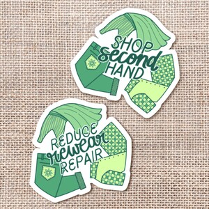 May include: Two die-cut stickers featuring shades of green. One sticker displays the text SHOP SECOND HAND, and the other displays REDUCE REWEAR REPAIR. Both designs incorporate illustrations of folded pants and fabric patterns in various green tones.