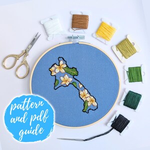 May include: A blue embroidery hoop with a floral design of a tropical island. The hoop is surrounded by spools of embroidery floss in various colors, including brown, white, yellow, green, and black. The text "pattern and pdf guide" is written in a blue circle.