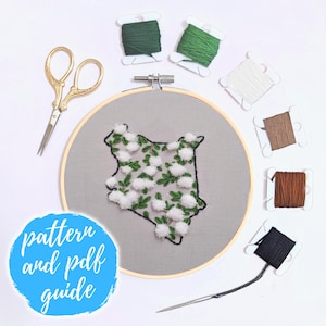 May include: Embroidery kit featuring a map of Kenya with white cotton balls and green embroidery floss. The kit includes a wooden embroidery hoop, scissors, and a needle. The text "pattern and pdf guide" is written on a blue circle.