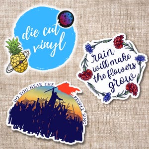 May include: Three die-cut vinyl stickers. The first sticker is blue with white text that says "die cut vinyl". The second sticker is white with a floral wreath and text that says "rain will make the flowers grow". The third sticker is black with a silhouette of people and text that says "Do you hear the people sing".
