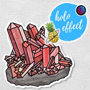 May include: A sticker featuring a cluster of pink and red crystals with a glittery texture. The crystals are set on a grey rock base. The sticker has a holographic effect and the text "holo effect" is written in blue on a blue circle.
