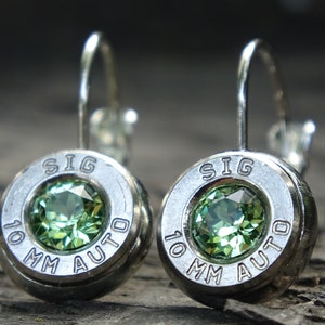 May include: A pair of silver bullet earrings with green gemstones. The earrings are marked "SIG 10 MM AUTO".