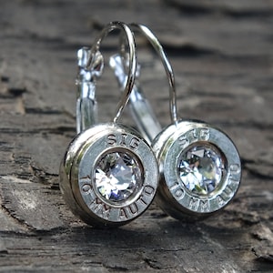 May include: Silver bullet earrings with clear crystal stones. The bullets are engraved with "SIG 10 MM AUTO".