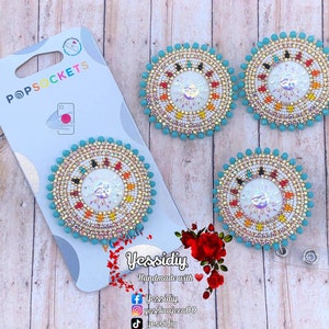 May include: Three turquoise and gold beaded suncatcher popsockets with a white iridescent center. The popsockets are handmade and feature a beaded design with a sun and rays.