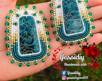 May include: A pair of green and white beaded earrings with a turquoise stone center. The earrings are handmade and feature a gold trim.