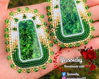 May include: A pair of green and white beaded earrings with a green stone center. The earrings are handmade and feature a gold trim.