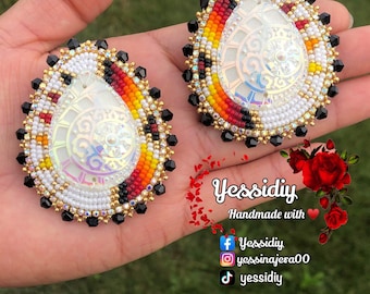 May include: A pair of teardrop-shaped earrings with a white iridescent center surrounded by black, gold, red, and orange beads. The earrings are handmade and feature a unique design.