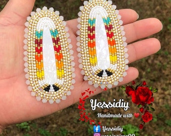 Può includere: Un paio di orecchini ovali con sfondo bianco e disegni di perline colorate. Gli orecchini sono fatti a mano e presentano una varietà di colori, tra cui rosso, giallo, arancione, blu e verde. Gli orecchini sono circondati da un bordo di perline dorate.