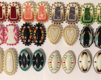 May include: A set of 12 pairs of beaded earrings. The earrings are made with various colors and patterns, including red, pink, white, black, green, and turquoise. The earrings are all oval shaped and have a gold trim.