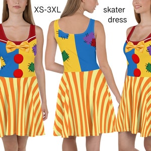 Puede incluir: Un vestido skater amarillo, azul y rojo con un diseño de payaso. El vestido tiene un lazo rojo, botones rojos y una falda a rayas. El vestido está disponible en tallas XS-3XL.