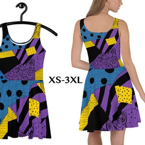 Op de afbeelding: Een mouwloze skaterjurk met een patchwork-ontwerp in blauw, paars, geel en zwart. De jurk wordt op een hanger getoond en door een persoon gedragen. De tekst "XS-3XL" is zichtbaar.