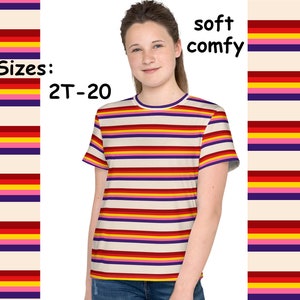 May include: A short-sleeved t-shirt with horizontal stripes in red, yellow, pink, purple, and cream colors. The shirt has a crew neck with a purple trim. The text "soft comfy" is on the right side of the image, and "Sizes: 2T-20" is on the left.