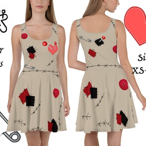 Puede incluir: Un vestido skater beige con un diseño de patchwork que presenta retazos de tela roja y negra, imperdibles, botones y un corazón rojo con un alfiler. El vestido tiene un escote redondo y es sin mangas. El texto "Skater dress" y "Sizes: XS-3XL" es visible en la imagen.