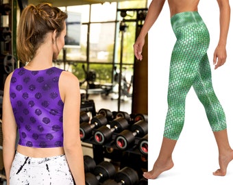 Puede incluir: Un top corto morado con un estampado floral oscuro y leggings con estampado blanco y negro. Las mallas tienen un diseño verde en forma de escamas. La imagen está tomada en un gimnasio con pesas en el fondo.