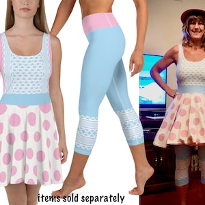 May include: A sleeveless dress and leggings set. The dress features a white bodice with blue floral and lace details, a light blue waistband, and a pink polka dot skirt. The leggings are light blue with a pink waistband and white lace trim.