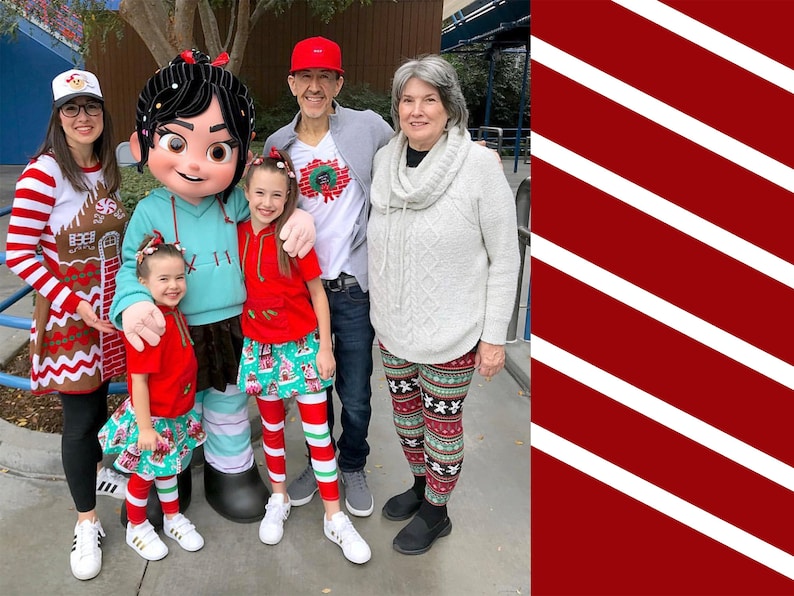 May include: A family of five pose for a photo with a character from the film Wreck-It Ralph. The character is wearing a blue and white outfit and has black hair. The family are wearing festive holiday attire, including red and white striped leggings, a gingerbread house sweater, and a red and white striped shirt. The character is holding a child in a red shirt and a green and white skirt.