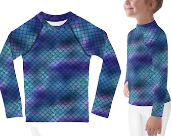 May include: A long-sleeved rash guard featuring a mermaid scale pattern in shades of blue, purple, and teal. The shirt has a mock neck and is designed for a comfortable fit. The scales have a shimmering effect, adding a touch of fantasy.