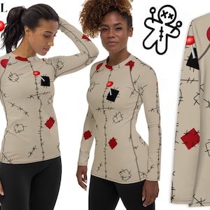 Puede incluir: Una camiseta de manga larga con fondo beige y un patrón de puntadas rojas y negras, que se asemeja a una muñeca vudú. La camiseta tiene cuello redondo y mangas largas. La camiseta está disponible en tallas XS-3XL.