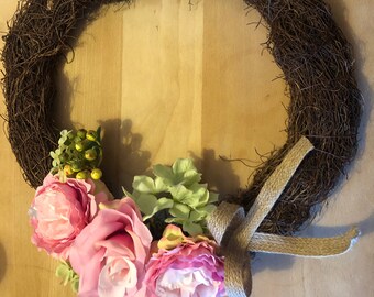 May include: A brown twig wreath decorated with pink and green artificial flowers and a burlap bow.