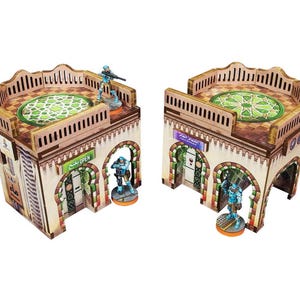Puede incluir: Dos edificios en miniatura detallados con puertas arqueadas y patios en la azotea. Los edificios están pintados en tonos marrones, blancos y verdes. Los tejados presentan tejas con intrincados patrones. Cada edificio tiene una figura en miniatura de pie delante de él.