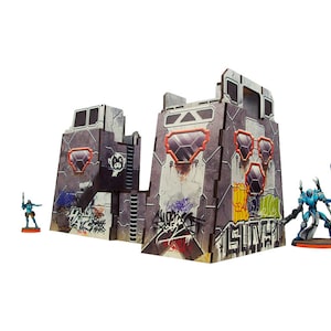Puede incluir: Un edificio modular gris, blanco y naranja con grafitis y ventanas. El edificio está hecho de cartón y está diseñado para juegos de mesa. Dos figuras en miniatura están de pie frente al edificio.