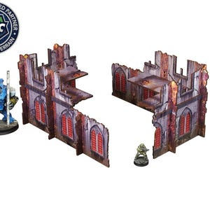 May include: Two ruined building sections made of cardboard, painted in shades of gray, brown, and red, with red window openings. The sections are designed for tabletop gaming.