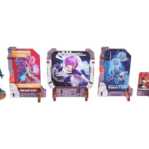 Op de afbeelding: Een verzameling miniatuurbeeldjes en displaykaarten. De beeldjes zijn in tinten blauw, oranje en wit. De displaykaarten bevatten illustraties in anime-stijl met tekst, waaronder het woord "Aristeia."