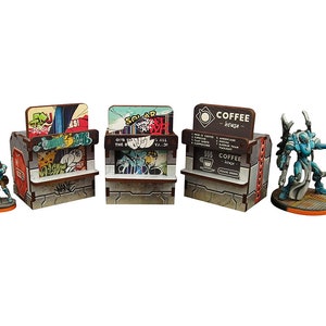 Op de afbeelding: Drie miniatuurhouten gebouwen met graffiti en een koffieshop-bord. Het koffieshop-bord heeft de tekst "COFFEE - house -" en somt verschillende soorten koffie op. Een blauwe robotfiguur met een zwaard staat voor de koffieshop.