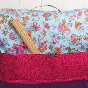 Puede incluir: Una funda para m&aacute;quina de coser de flores azules y rosas con un bolsillo de tela rosa y una regla y unas tijeras en el interior.