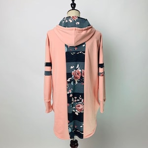May include: A pink hooded sweatshirt with a floral and striped pattern on the back. The sleeves have a striped pattern.