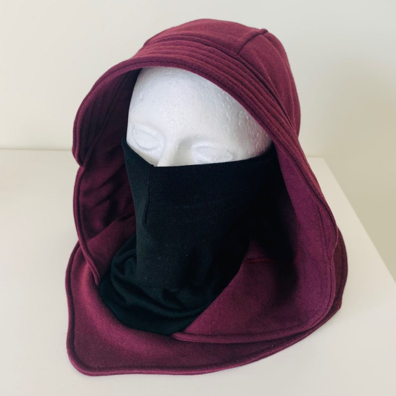 May include: A maroon hooded sweatshirt with a black face mask. The hood is pulled up and the mask is covering the face.