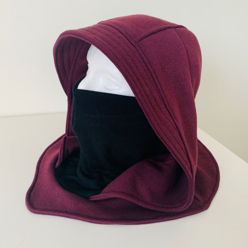May include: A burgundy hooded neck warmer with a black face mask. The hood is lined with a soft, plush fabric.