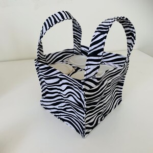 May include: A black and white zebra print fabric tote bag with two handles. The bag is filled with white containers.