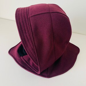 May include: A burgundy hooded hat with a wide brim and a soft, quilted texture.