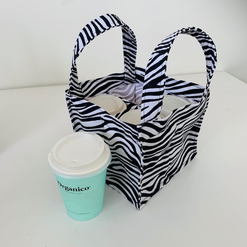 May include: A black and white zebra-print fabric tote bag with two handles. The bag is filled with four white cups and has a teal-colored cup with the text "Organico" on the front.
