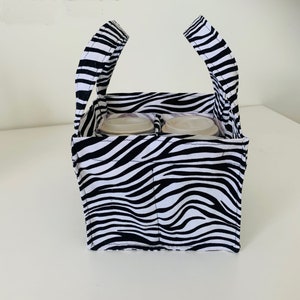 May include: A black and white zebra print fabric tote bag with two handles. The bag has four compartments for holding cups or cans.