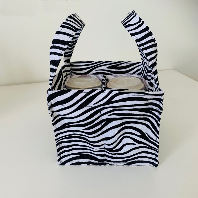 May include: A black and white zebra print fabric tote bag with two handles. The bag has four compartments for holding cups or cans.