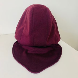 May include: A burgundy hooded hat with a wide brim. The hat is made of a soft, stretchy fabric and has a simple design.