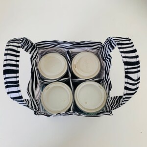 May include: A black and white striped fabric tote bag with four white cups inside. The tote bag has two handles and is designed to carry multiple cups.
