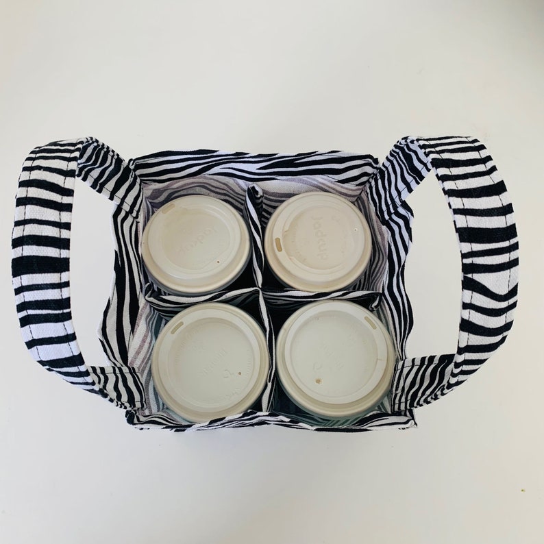 May include: A black and white striped fabric tote bag with four white cups inside. The tote bag has two handles and is designed to carry multiple cups.