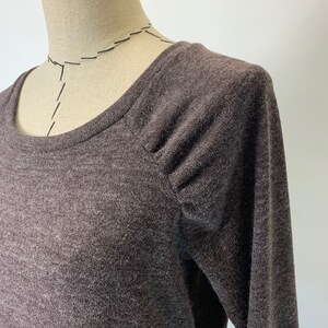 以下が含まれることがあります： 丸首で肩が少しパフスリーブになった、茶色の長袖シャツです。