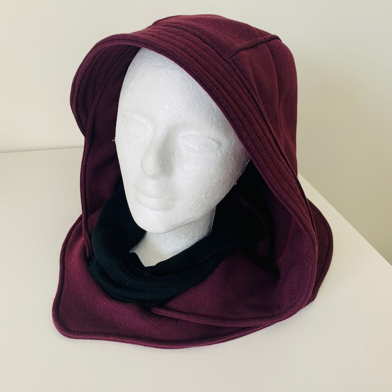 May include: A burgundy hooded cowl with a black fleece lining. The cowl is made of a soft, comfortable fabric and has a relaxed fit.