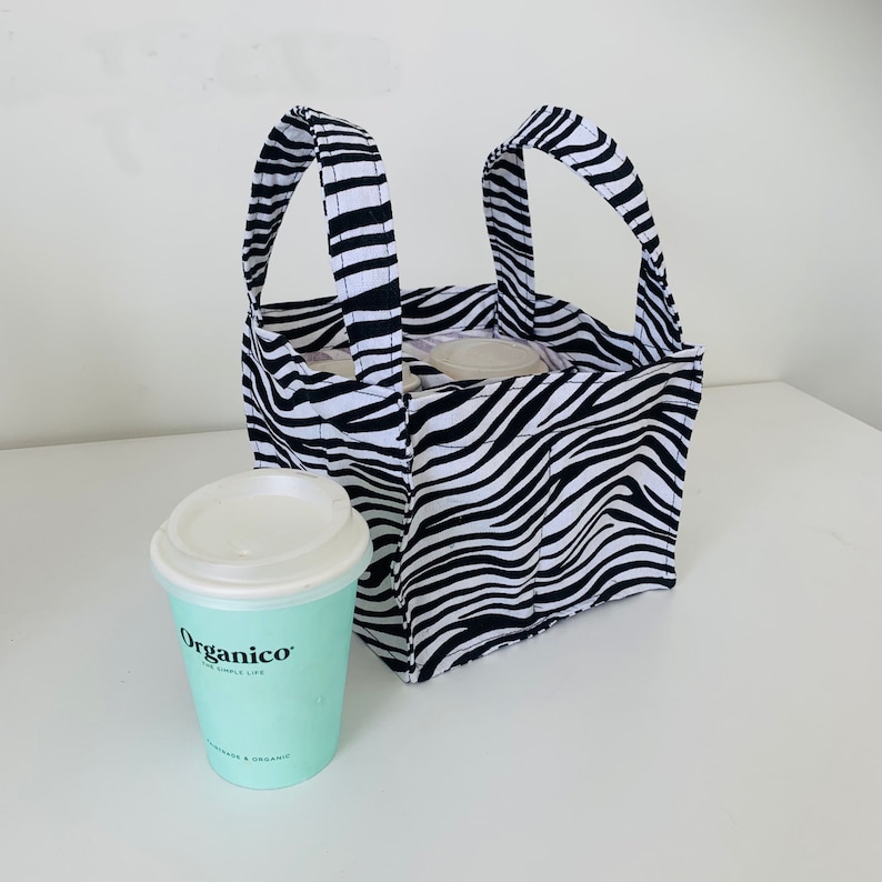 May include: A black and white zebra print tote bag with two handles. The bag is filled with four cups and a light blue cup with the word "Organico" printed on it.